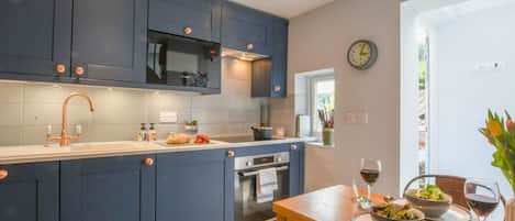 A modern kitchen with dark blue cabinets, a stainless steel sink, and a dining area with a table set for two.