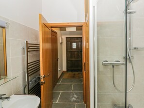 Un baño con ducha, lavamanos y una puerta de madera que da a un pasillo.