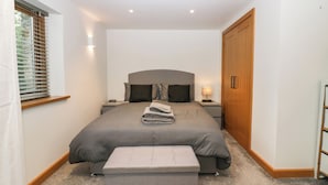 Quarto com uma cama grande, mesa de cabeceira com luminária, guarda-roupa de madeira e janela com persianas.