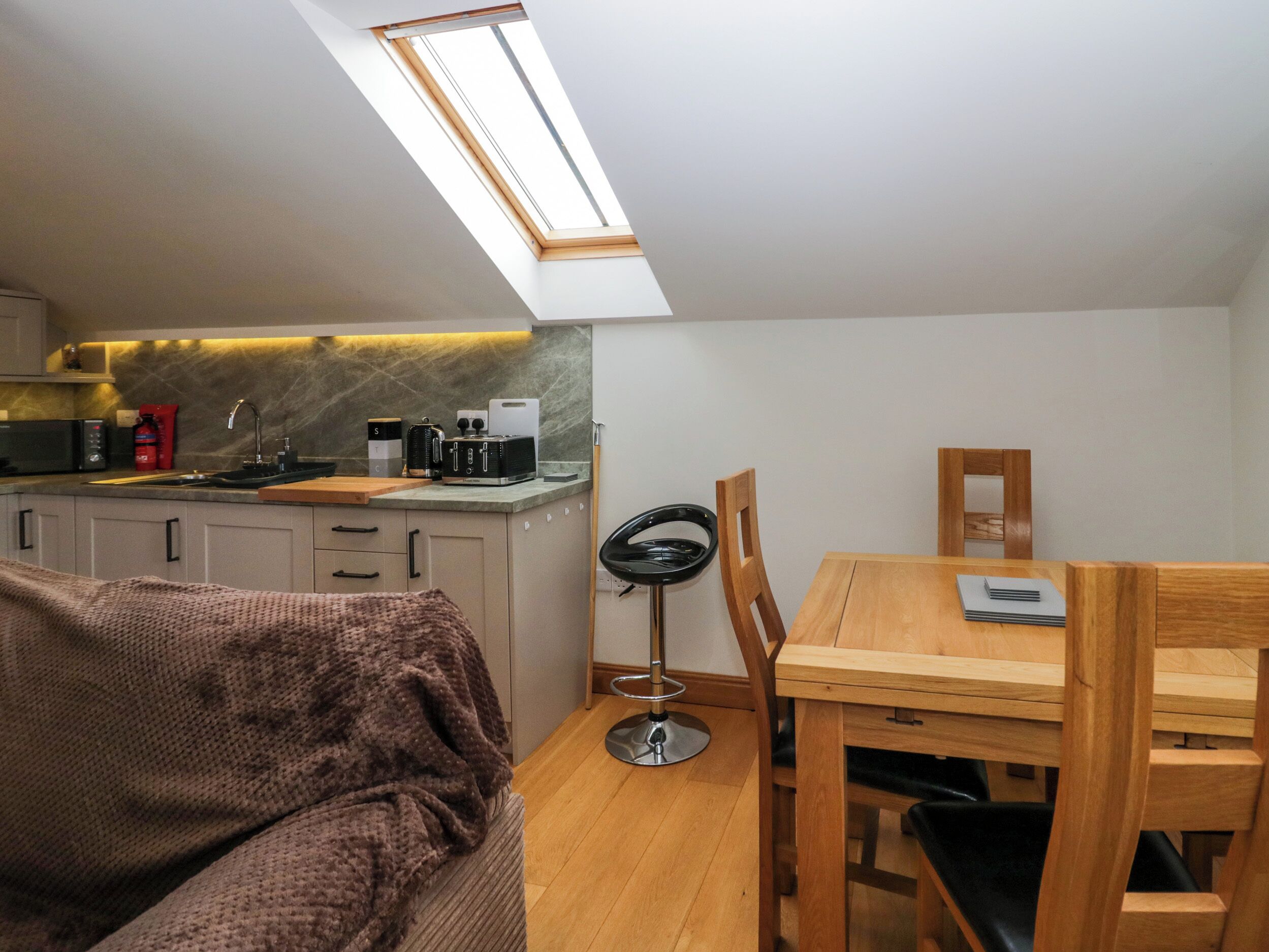 Una cocina compacta con tragaluz, un comedor con mesa y sillas, y una zona de estar acogedora con un sofá.