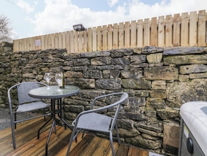 Un muro de piedra con cerca de madera, una mesa redonda con sillas y un jacuzzi.