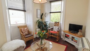 A cozy living room with a wicker chair, a glass coffee table, a television, and a radiator. - Belmont House (Windermere)