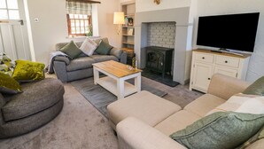 A cozy living room with a sofa, armchair, coffee table, fireplace, television, and a bookshelf. - Edmunds Cottage (Bedale)