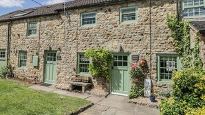 A stone cottage with green shutters, a small garden, and a sign indicating 'Edmunds Cottage'. - Edmunds Cottage (Bedale)