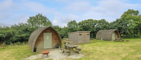 Three wooden cabins with a picnic table and a wheelbarrow in the foreground.