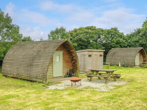 A campsite with wooden cabins, a picnic table, and a wheelbarrow. - Rabbit Warren @ Penbugle Organic Farm (Liskeard)