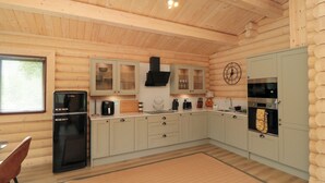 Een keuken in blokhutstijl met houten wanden en plafond, een koelkast, kasten, een fornuis en een klok aan de muur.