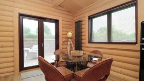 Een houten cabinestijl interieur met een ronde glazen tafel, vier bruine stoelen, een vloerlamp en een groot raam met jaloezieën.