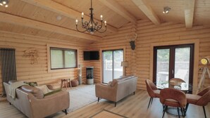 Een blokhut interieur met een open haard, twee banken, een eettafel met stoelen en een kroonluchter.