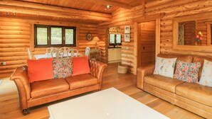 Interno di una baita in legno con due divani in pelle, un tavolino da caffè bianco e una zona pranzo con sedie e tavolo.