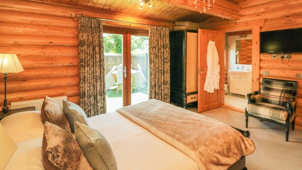 Camera da letto in una baita di legno con un letto, un lampadario, una televisione e vista all'esterno.