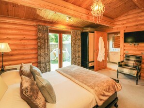 A wooden cabin bedroom with a bed, a chandelier, a television, and a view of the outside. - Roseberry Lodge 3 (Middlesbrough)