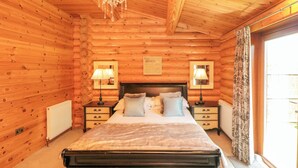 Camera da letto in una baita di legno, con un letto grande, due comodini con lampade, un lampadario e una finestra con tende.