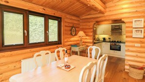 Interno di una baita in legno con tavolo da pranzo, sedie, angolo cottura e un orologio appeso al muro.