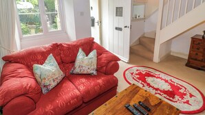 A living room with a red sofa, a wooden coffee table, and a red and white patterned rug. - 4 Lansdown Cottages (Cheltenham)