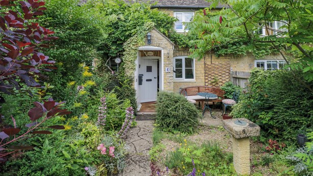 A stone house with a garden, a bench, and a clock on the door. - 4 Lansdown Cottages (Cheltenham)