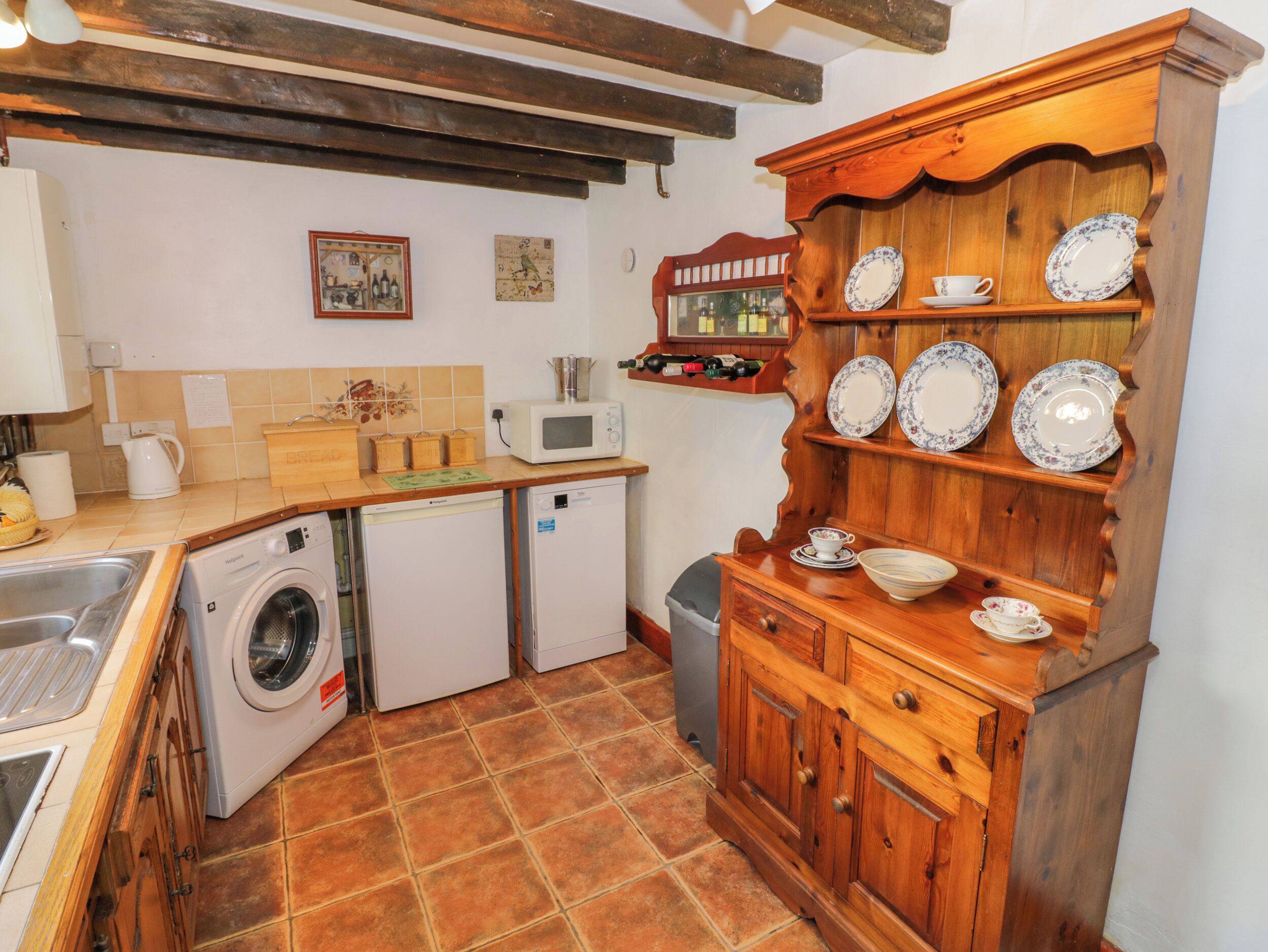 A compact kitchen with a washing machine, a microwave, a sink, and a wooden cabinet with dishes.