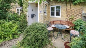 A stone house with a wooden bench and a metal table in the garden. - 4 Lansdown Cottages (Cheltenham)