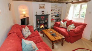 A cozy living room with red sofas, a wooden coffee table, and a fireplace. - 4 Lansdown Cottages (Cheltenham)