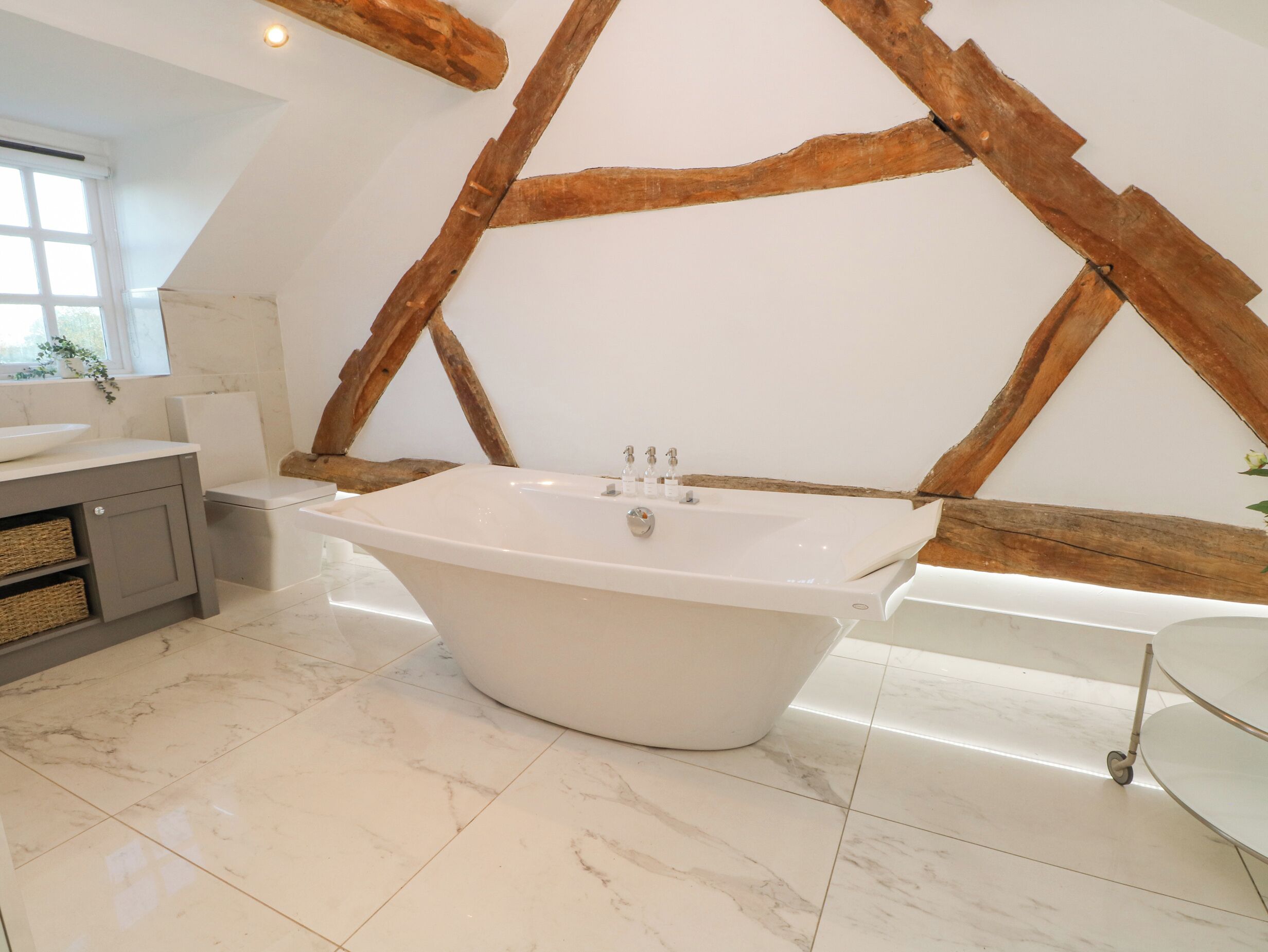 A modern bathroom with a freestanding bathtub, marble flooring, and exposed wooden beams.