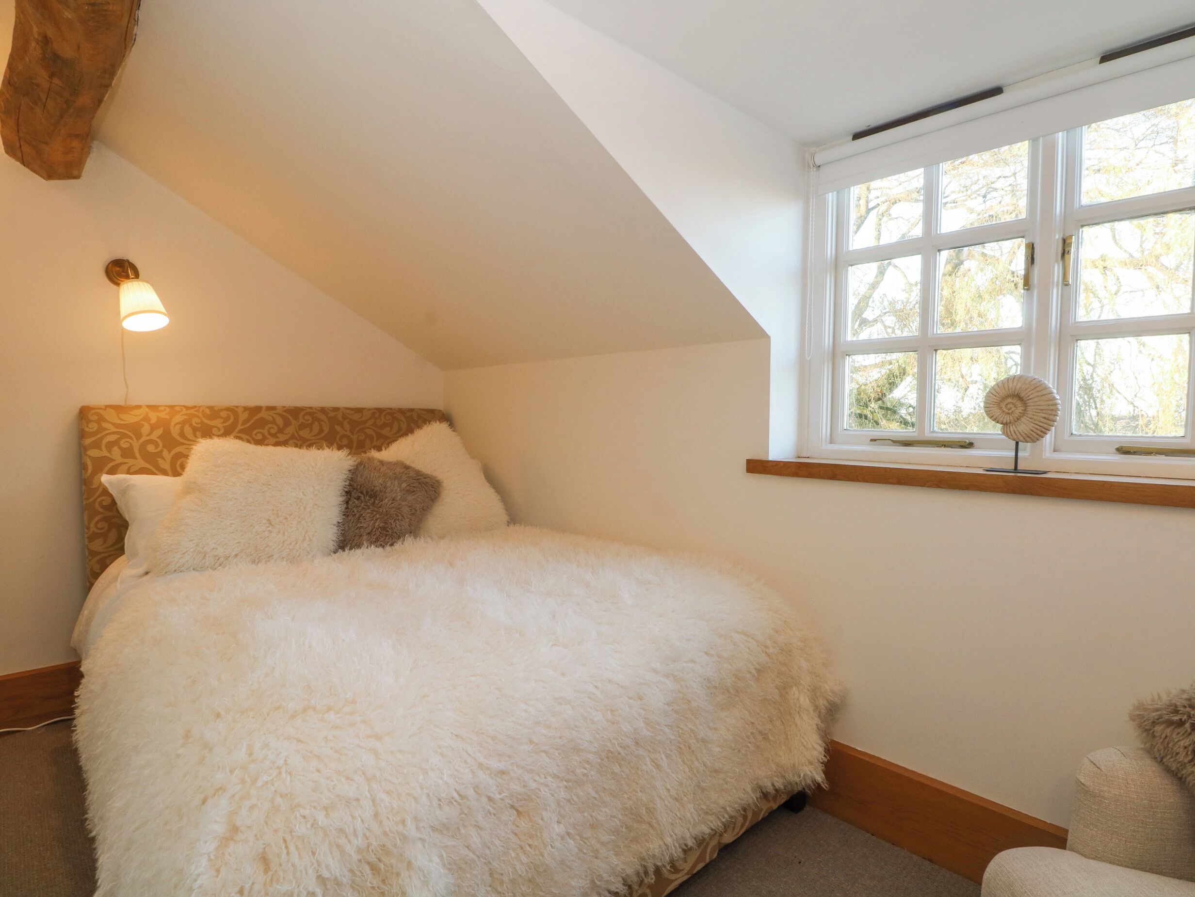 Un dormitorio con cama, ventana con vistas y lámpara de pared.