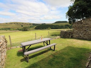 A picnic table in a grassy field with a stone wall and a stone building in the background. - Middlefell View Cottage (Alston)