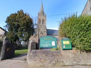 A church with a tall spire, a stone wall, and a green signboard with information. - Middlefell View Cottage (Alston)