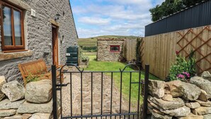A stone house with a stone wall, a wooden door, a window, and a gate. - Middlefell View Cottage (Alston)