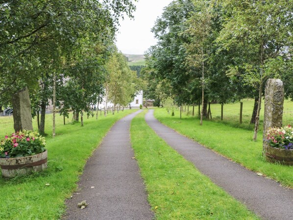 A pathway flanked by trees and flower beds, leading to a distant white building. - Middlefell View Cottage (Alston)