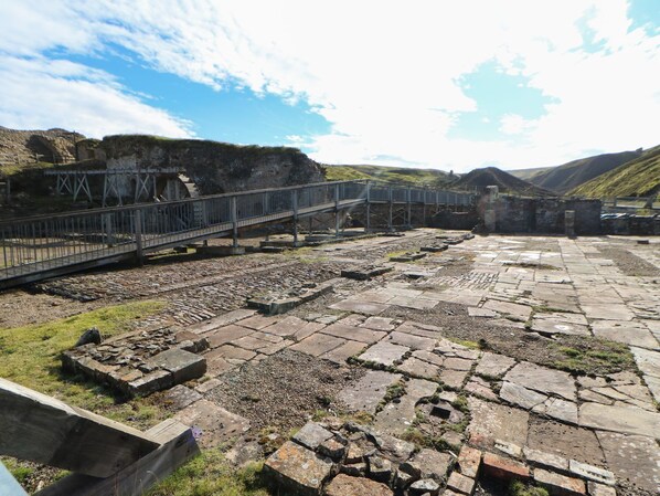 An outdoor archaeological site with stone ruins and a metal bridge.