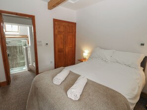 A bedroom with a bed, a nightstand, a lamp, a wooden wardrobe, and a bathroom visible through an open door. - Wellhope View Cottage (Alston)