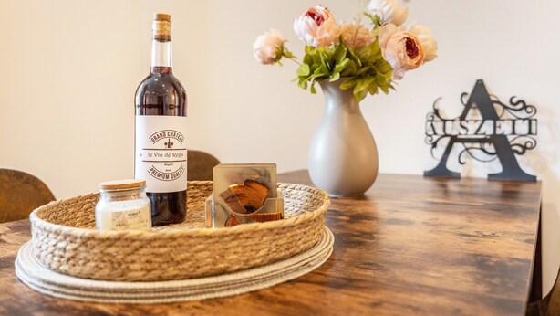 Una botella de vino, un florero con flores y una letra decorativa sobre una mesa de madera.