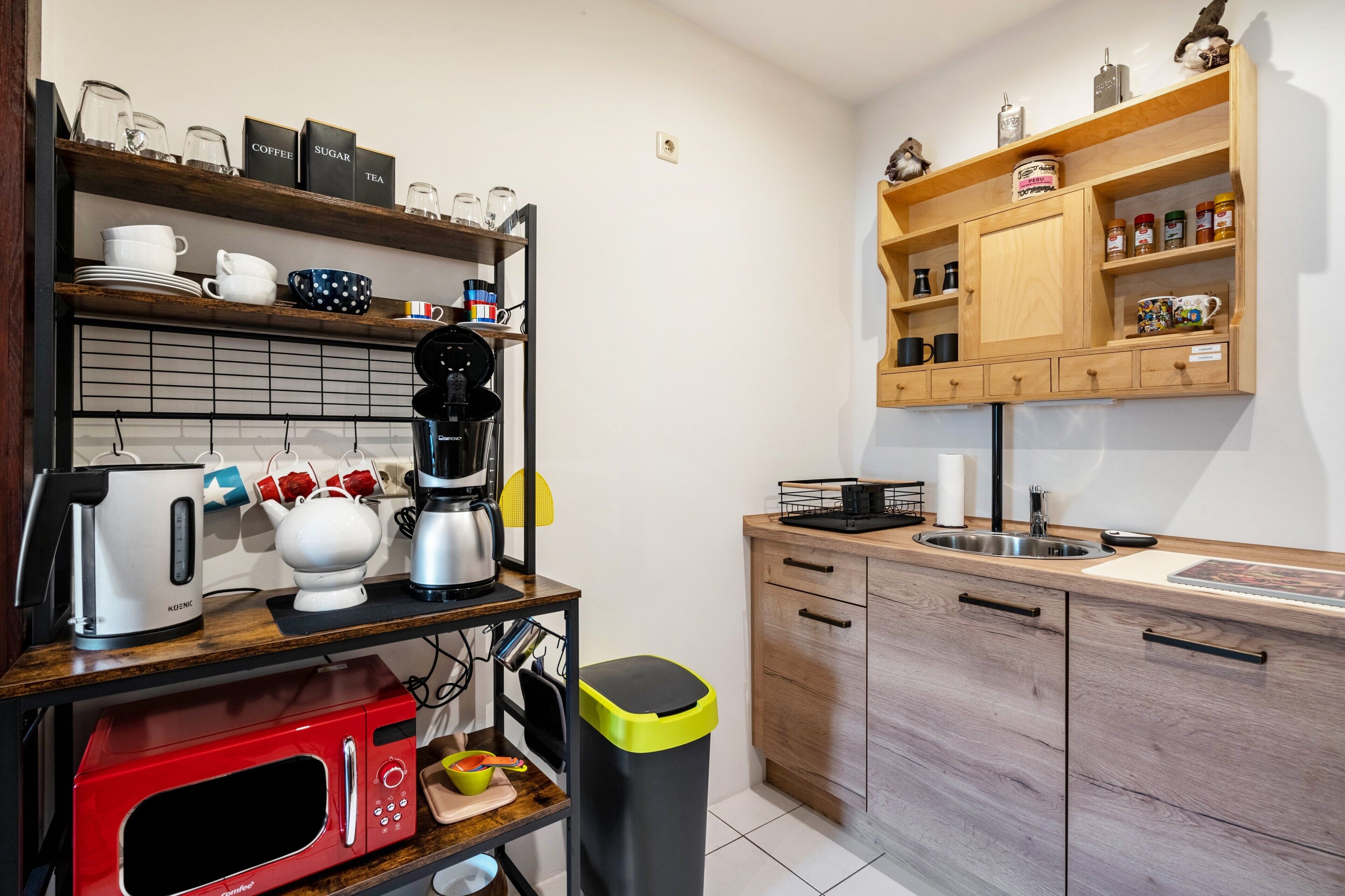 Cocina compacta con cafetera, hervidor, microondas y cubo de basura.