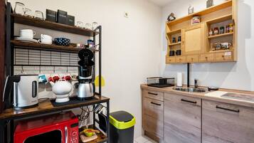 Cocina compacta con cafetera, hervidor, microondas y cubo de basura.