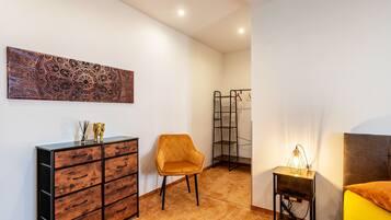 Une chambre à coucher comprenant un lit, une table de chevet, une chaise, une commode et une œuvre d’art murale.