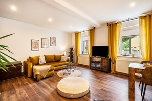 A living room with a sofa, ottoman, coffee table, TV, and dining area with yellow curtains.