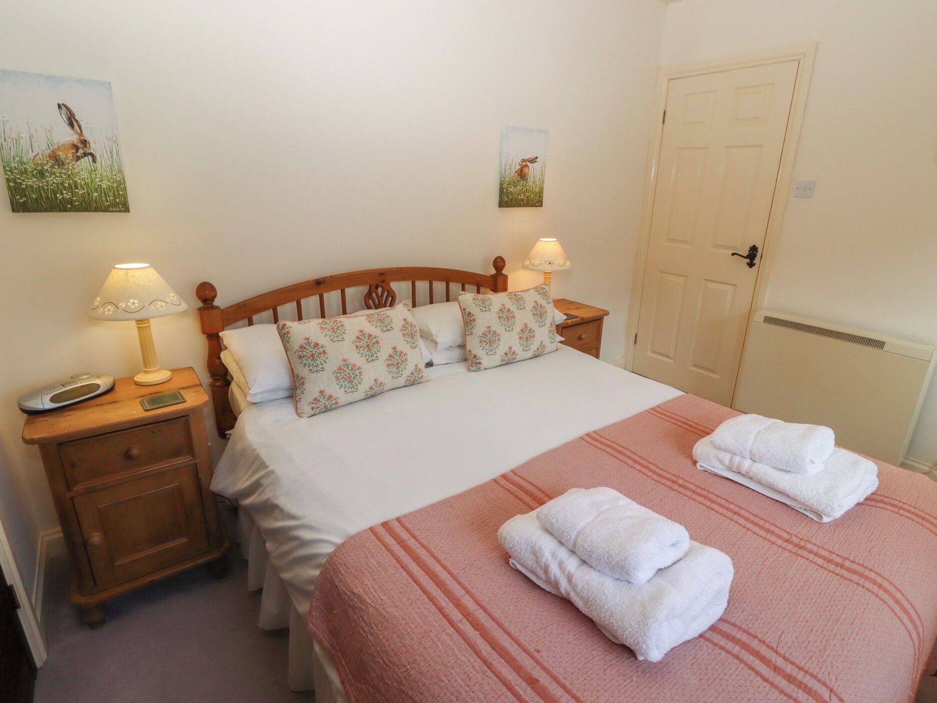 A neatly made bed with floral pillows, a bedside lamp, and a bedside table with a phone and a small drawer.