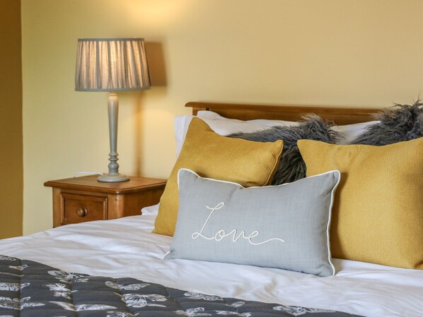 A neatly made bed with a floral-patterned bedspread, a lamp on a bedside table, and two pillows with one labeled "Love". - St Edmunds House (Bedale)