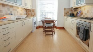 A compact kitchen with a washing machine, a dining table with chairs, and a stove. - Captain's Rest (Porthmadog)