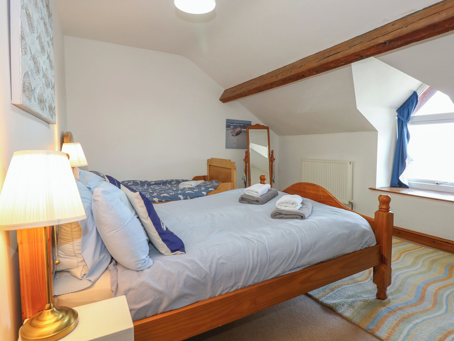A bedroom with a wooden bed, two bedside lamps, a mirror, and a window with curtains.