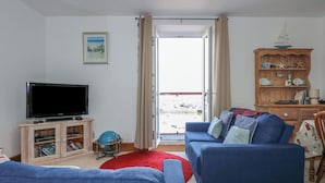 A living room with a television, a globe, a red rug, and a wooden cabinet with nautical decorations. - Captain's Rest (Porthmadog)