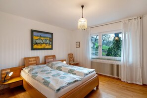 Une chambre à coucher avec un lit en bois, une table de chevet avec une lampe, une fenêtre avec des rideaux et un tableau accroché au mur.