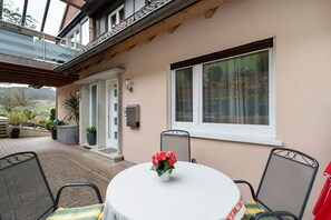 Une terrasse avec une table ronde, des chaises et un pot de fleurs.