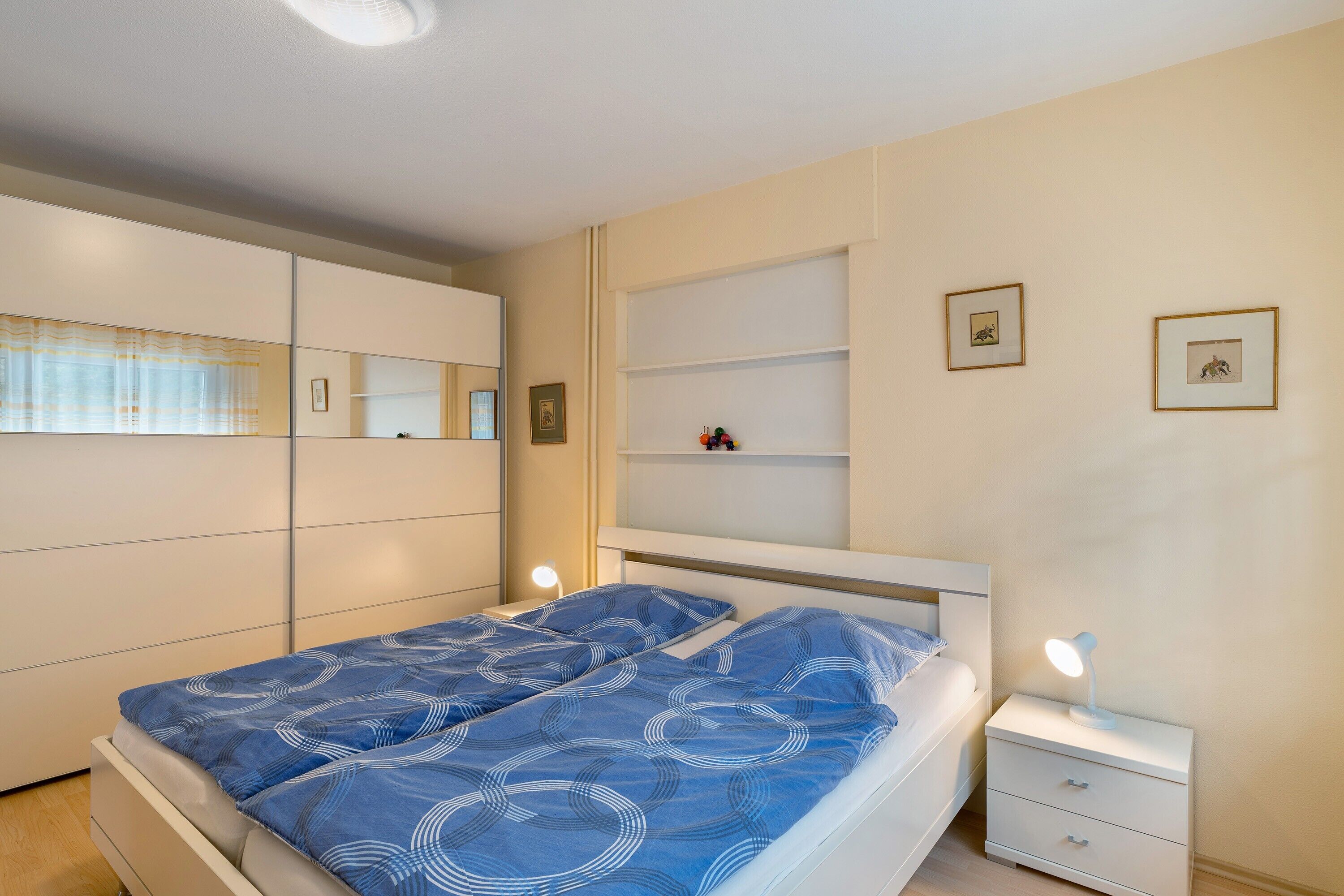 Ein Schlafzimmer mit einem Bett, Nachttischen, Ablageflächen und Regalen an der Wand.
