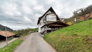 Eine Landstraße führt zu einem Haus mit einem geneigten Dach und einem Balkon.