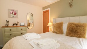A neatly made bed with white linens and a fluffy pillow, a dresser with a mirror and framed photos, and a wall-mounted deer head decoration. - Loft Cottage (Bedale)