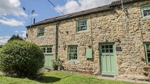A stone cottage with green doors and windows, a stone roof, and a clear sky. - Loft Cottage (Bedale)
