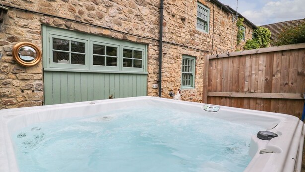 A stone building with a wooden fence, a hot tub, and a wooden door. - Loft Cottage (Bedale)