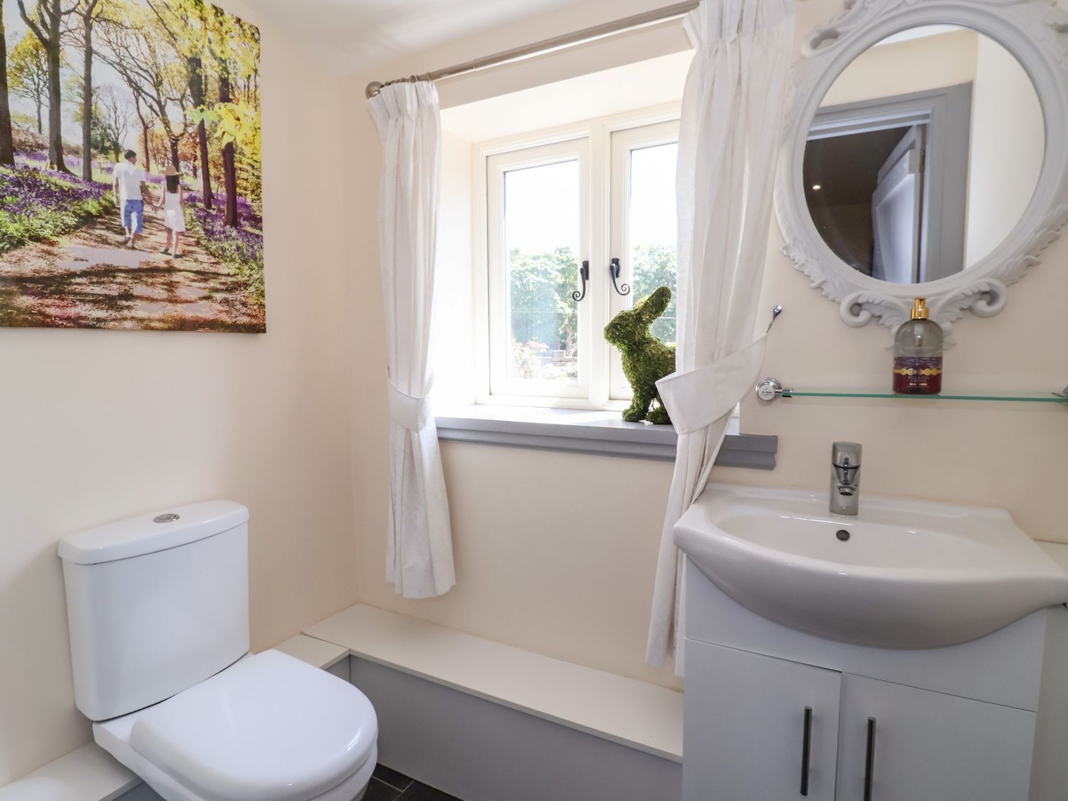 Un baño con inodoro, lavabo, espejo y ventana con cortina.