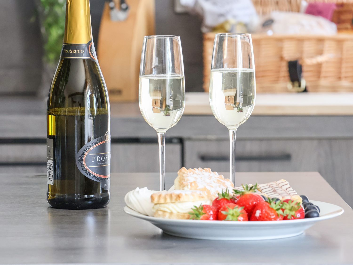 A bottle of Prosecco wine, two glasses of wine, and a plate with pastries and strawberries.